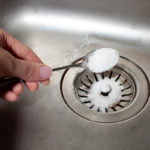 A spoon scooping drain chemicals into a kitchen drain